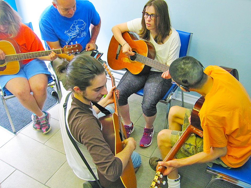 Il y a deux jeunes de la fondation des aveugles qui sont assis avec une guitare à la main et un professeur également avec une guitare qui est en train d'expliquer à un jeune où mettre ses mains sur la guitare.