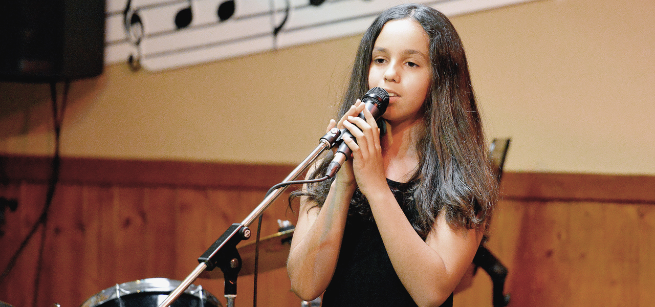Fille de 10-12 ans qui chante devant un public au spectacle organisé par Musique O Max.