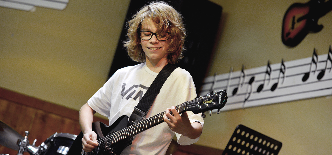 Jeune adolescent jouant de la guitare électrique lors du spectacle organisé par Musique O Max.